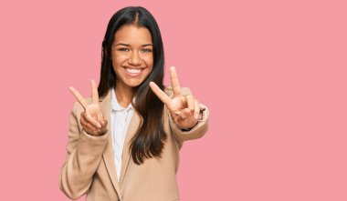 Güzel İspanyol kadın iş ceketi giyiyor gülümsüyor kameraya bakıyor zafer işareti yaparken parmaklarını gösteriyor. İki numara.. 