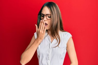 Genç esmer kadın gündelik kıyafetler ve gözlük takmış. Ağzı eliyle kapatmaktan sıkılmış. Huzursuz ve uykulu.. 