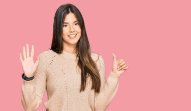 Kış süveteri giyen genç esmer kadın altı numarayı gösterip işaret ederken kendinden emin ve mutlu bir şekilde gülümsüyor.. 