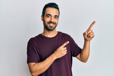 Gündelik kıyafetler giyen genç İspanyol adam gülümseyip kameraya bakıyor ve iki eliyle ve parmaklarıyla kenarı işaret ediyor.. 
