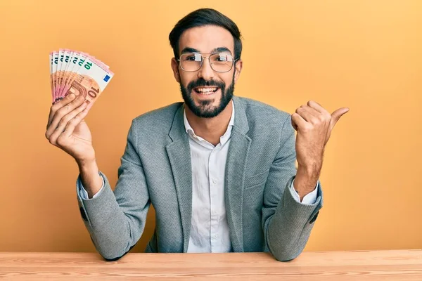 Joven Hispano Sosteniendo Billetes Euros Apuntando Con Pulgar Hacia Costado — Foto de Stock