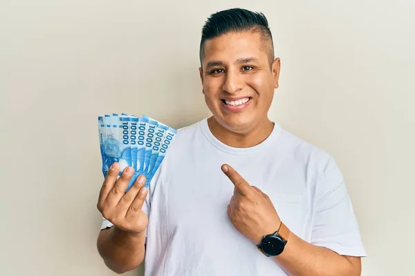 Młody Latynos Trzyma 10000 Chilijskich Pesos Uśmiechając Się Szczęśliwy Wskazując — Zdjęcie stockowe