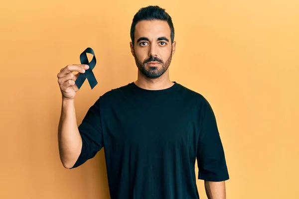 Young Hispanic Man Holding Black Ribbon Thinking Attitude Sober Expression — Stock Photo, Image