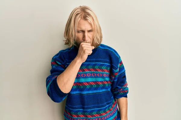 カラフルな冬のセーターを着て長い髪を持つ白人の若い男は具合が悪く 風邪や気管支炎の症状として咳をします ヘルスケアの概念 — ストック写真