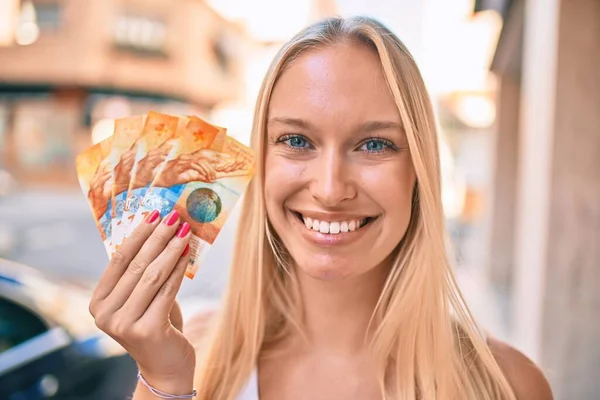 Młoda Blondynka Uśmiechnięta Szczęśliwa Trzymając Szwajcarskie Banknoty Frankowe Spacerując Mieście — Zdjęcie stockowe