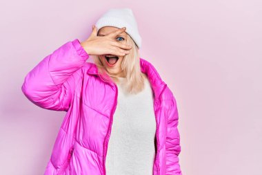 Güzel, beyaz, sarışın kadın yün şapka ve kışlık palto giyiyor. Şok olmuş bir şekilde yüzünü ve gözlerini kapatıyor. Utanmış bir ifadeyle parmaklarının arasından bakıyor.. 