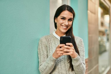 Genç İspanyol kadın şehirde akıllı telefon kullanarak mutlu bir şekilde gülümsüyor..