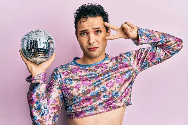 Parlak disko topunu tutan yakışıklı bir adam cahil ve kafası karışmış bir ifade takınıyor. şüphe kavramı. 