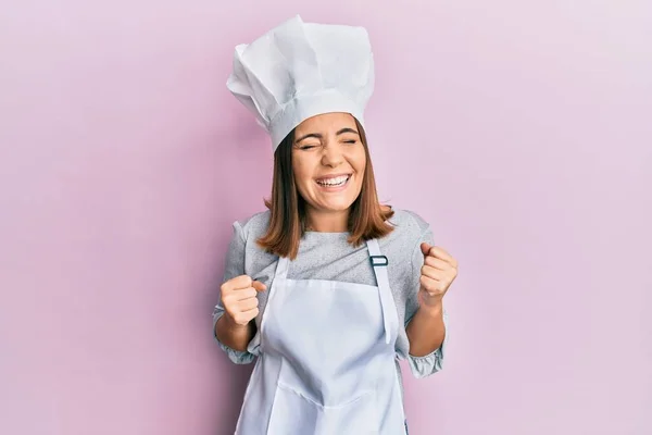 プロの料理の制服を身に着けている若い美しい女性は腕を上げ 笑顔と成功のために叫んで勝者のジェスチャーを行うと非常に幸せと興奮帽子 お祝いのコンセプト — ストック写真