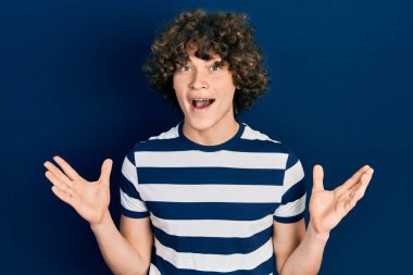 Yakışıklı, çizgili tişört giyen, çılgın kutlamalar yapan kolları açık, gözleri açık, çılgın bir başarıyı kutlayan genç bir adam. Kazanan konsept 