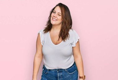 Genç ve cüsseli bir kadın, günlük beyaz tişört giyiyor, kameraya seksi bir ifadeyle bakıyor, neşeli ve mutlu bir yüzle.. 