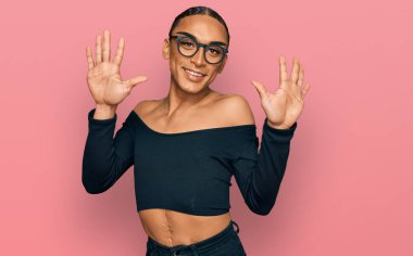 Makyaj yapan, uzun saçlı, kadın kıyafetleri giyen İspanyol transseksüel adam on numaralı parmaklarıyla onu gösterirken kendinden emin ve mutlu gülümsüyor.. 