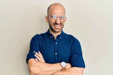 Gündelik kıyafetler ve gözlük takan genç İspanyol adam kameraya bakarken kollarını kavuşturup gülümsüyor. pozitif kişi. 