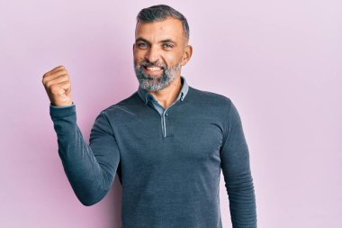 Orta yaşlı, sıradan kıyafetler giyen, mutlu yüzlü, gülümseyen ve baş parmağıyla yan tarafı gösteren yakışıklı bir adam.. 