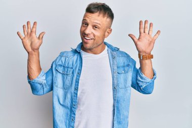 Yakışıklı, sıradan kot ceket giyen kaslı adam on numarayı gösterip işaret ederken kendinden emin ve mutlu bir şekilde gülümsüyor.. 