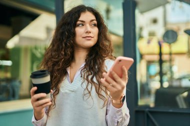Genç İspanyol kadın akıllı telefon kullanıyor ve şehirde kahve içiyor..