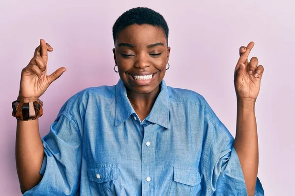 身穿休闲装的年轻的非洲裔美国女人 带着希望和闭上的眼睛 微笑着交叉着指尖 幸运与迷信的概念 — 图库照片