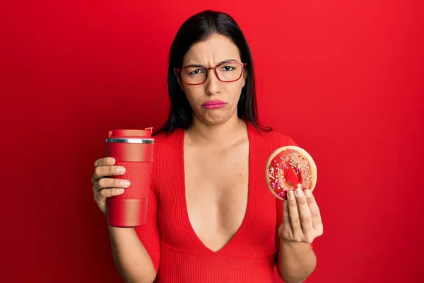 若いラテン語の女性のドーナツを食べ コーヒーを飲んで懐疑的で緊張し 問題のために動揺を眉をひそめる 否定的な人 — ストック写真