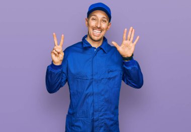 Sakallı, inşaatçı tulumu giyen kel bir adam yedi numaralı parmaklarıyla kendini gösterip gülümserken mutlu ve kendinden emin.. 