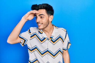Gündelik kıyafetler giyen genç İspanyol adam çok mutlu ve gülümsüyor. Elleri başının üzerinde uzaklara bakıyor. arama kavramı. 