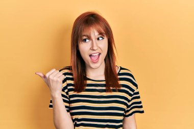 Kızıl saçlı, çizgili tişört giyen genç bir kadın baş parmağını kaldırmış, ağzı açık bir şekilde gülümsüyor. 