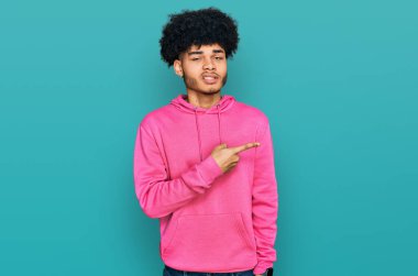 Afro saçlı, pembe kazaklı, endişeli, endişeli ve şaşırmış ifadesiyle endişeli ve gergin genç Afro-Amerikalı bir adam. 