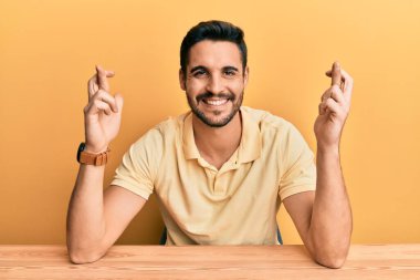 Gündelik giysiler giymiş genç İspanyol adam masanın üzerinde oturmuş umut ve gözler kapalı bir şekilde gülümseyerek el sallıyor. Şans ve batıl inançlar. 