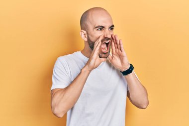Genç kel adam, günlük beyaz tişört giyip elleri ağzında kızgın bir şekilde bağırıyor. 