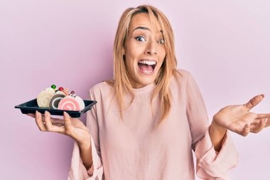 Güzel sarışın kadın pasta tatlısı tutuyor başarıyı mutlu bir gülümsemeyle ve kazanan yüz ifadesiyle kutluyor. 