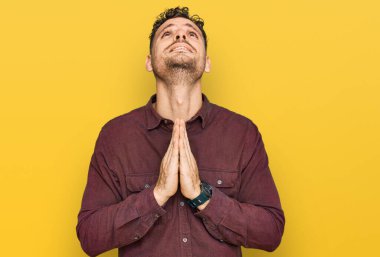 Gündelik giysiler giyen genç İspanyol adam elleri bağlı yalvarıyor ve dua ediyor. Yüzünde umut ifadesi var. Çok duygusal ve endişeli. Yalvarıyor. 