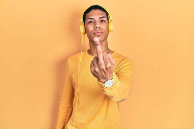 Young african american guy listening to music using headphones showing middle finger, impolite and rude fuck off expression 