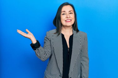 Orta yaşlı İspanyol kadın iş kıyafetleri giyiyor neşeli bir şekilde gülümsüyor ve avuç içi kameraya bakıyor.. 