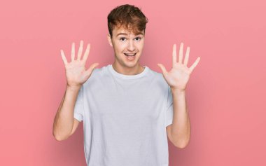 Beyaz günlük tişört giyen genç beyaz bir adam on numarayı gösterip işaret ederken kendinden emin ve mutlu bir şekilde gülümsüyor.. 