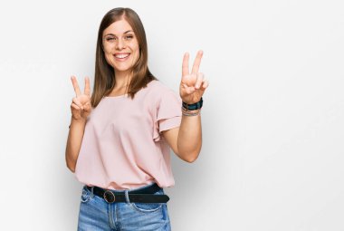 Gayri resmi giyinmiş, gülümseyen, parmaklarını zafer işareti yaparken gösteren güzel beyaz kadın. İki numara.. 