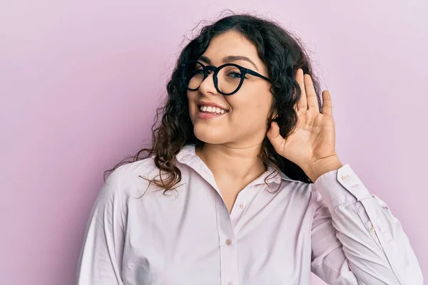 噂やゴシップに耳を傾け耳の上に手で笑みを浮かべてカジュアルな服や眼鏡を着て巻き毛を持つ若いブルネットの女性 聴覚障害の概念 — ストック写真