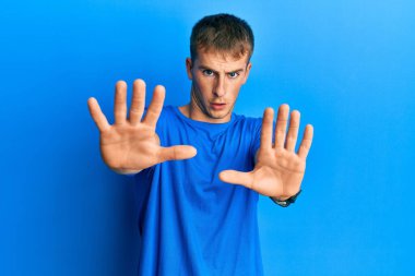 Kafkasyalı genç bir adam günlük mavi tişört giyiyor. Avuçlarıyla jestleri durduruyor. Öfkeli ve hayal kırıklığı dolu bir ifade takınıyor. 