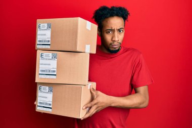 Sakallı genç Afro-Amerikan bir adam teslimat paketlerini kuşkucu ve gergin tutuyor, sorun yüzünden surat asıyor. negatif kişi. 