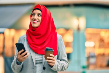 Genç Arap iş kadını akıllı telefon kullanıyor ve şehirde kahve içiyor..