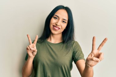 Gündelik tişört giyen genç İspanyol kız kameraya bakıp zafer işareti yapıyor. İki numara.. 