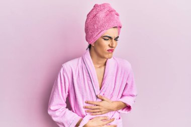 Kadın elbisesi giyen genç adam duş havlusu ve eli karnında bornoz giyerek makyaj yapıyor çünkü hazımsızlık, acı veren hastalıklar kendini iyi hissetmiyor. Ağrı kavramı. 