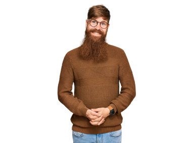 Genç İrlandalı kızıl adam, günlük kıyafetler ve gözlük takıyor ve elleri birarada ve mutlu ve gevşek gülümseyerek parmaklarını çapraz yapıyor. Başarı ve iyimserlik 