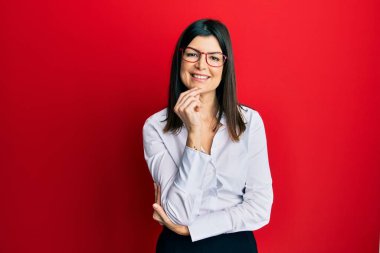 İş gömleği ve gözlük takan genç İspanyol kadın kameraya kollarını kavuşturup gülümseyerek ve çenesini kaldırarak bakıyor. Olumlu düşünmek. 