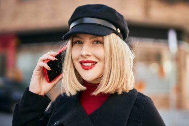 Genç sarışın kadın gülümsüyor. Şehirdeki akıllı telefondan konuşuyor..