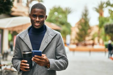 Genç Afrikalı Amerikalı adam akıllı telefon kullanıyor. Şehirde kahve içiyor.