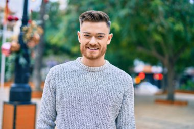 Genç beyaz adam parkta mutlu bir şekilde gülümsüyor..