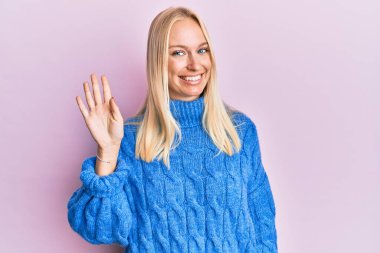 Kışın yün kazak giyen genç sarışın kız kendini beğenmiş ve mutlu bir şekilde gülümserken parmaklarıyla dört numarayı gösteriyor.. 