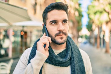 Ciddi bir suratı olan genç İspanyol bir adam şehirde akıllı telefondan konuşuyor..