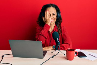 Güzel orta yaşlı bir kadın radyo stüdyosunda çalışıyor. Bir gözünü eliyle kapatıyor. Yüzünde kendine güvenen bir gülümseme ve sürpriz bir duygu var.. 