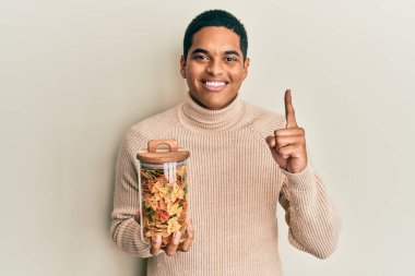 Genç yakışıklı İspanyol adam elinde farfalle makarna kavanozuyla gülümsüyor bir fikir veya soru işareti ile mutlu bir yüzle, bir numara 