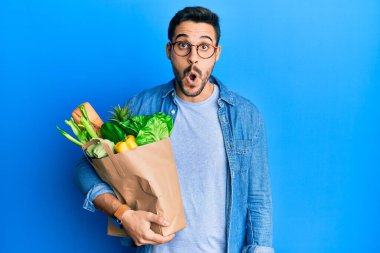 Elinde ekmek ve bakkaliye dolu kağıt torba tutan genç İspanyol adam şaşkınlık ve şaşkınlık içinde ağzı açık kalmış, imansız yüz. 